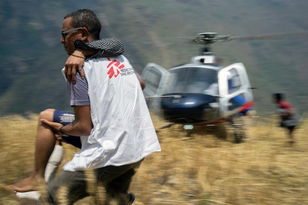 Maila Gurung, 26, is assisted off of a helicopter by MSF Dr. Hanni when returned home to Diol village, Gorkha District, Nepal on May 21 2015. Maila had been evacuated to the MSF hospital in Arughat Bazaar where his broken leg was treated. photo: Brian Sokol/Panos Pictures 