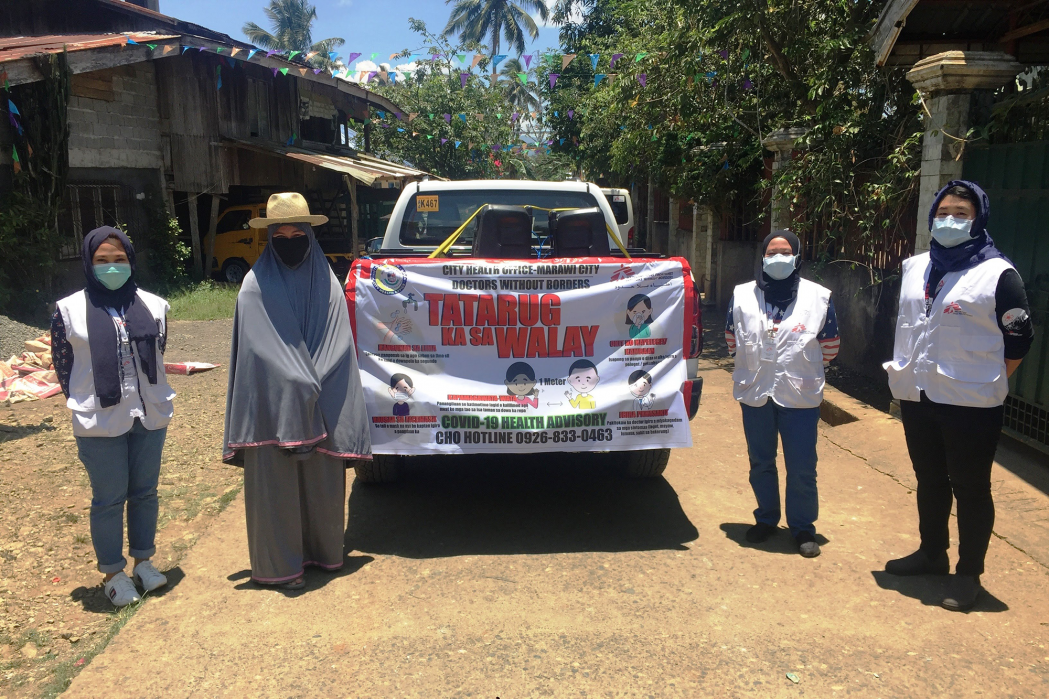The barangay (village) leader (lady with the hat) and MSF staff take a break during our mobile information drive. Our roving vehicle blasts health promotion messages around Marawi City. The tarpaulin reads "stay at home" in Marawi's language, Maranao. ©Gilbert G. Berdon