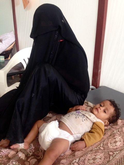 Fatima sits on the bed next to her 18-month-old son Ishaq