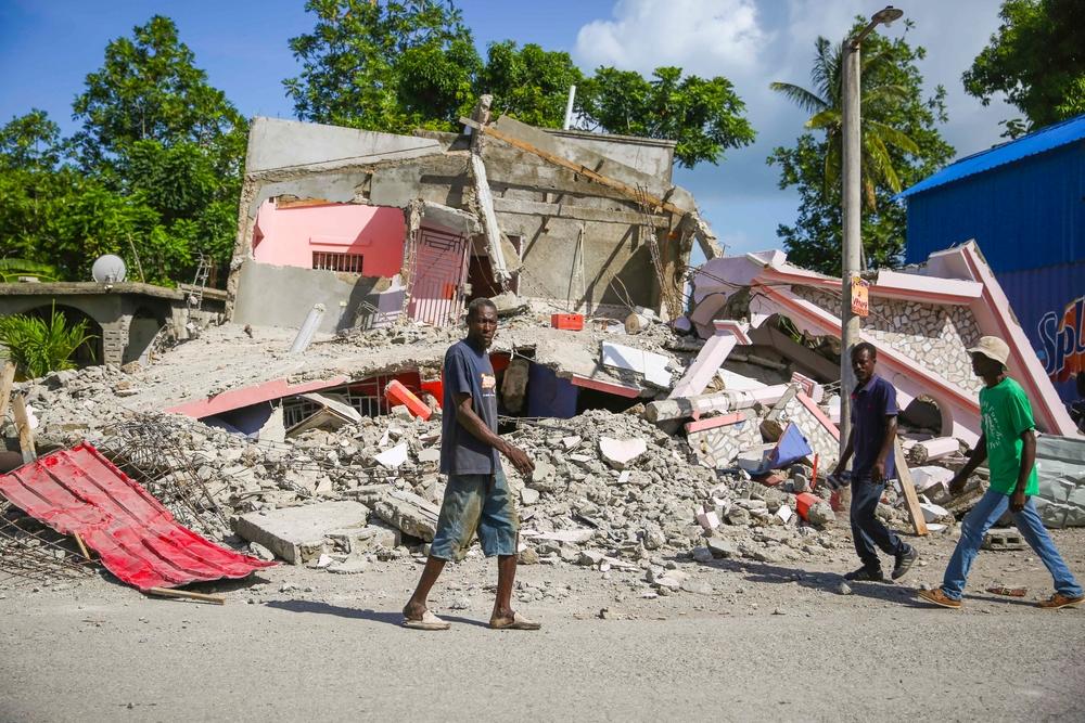 People walking in front of a destroyed building in a street of Les Cayes.