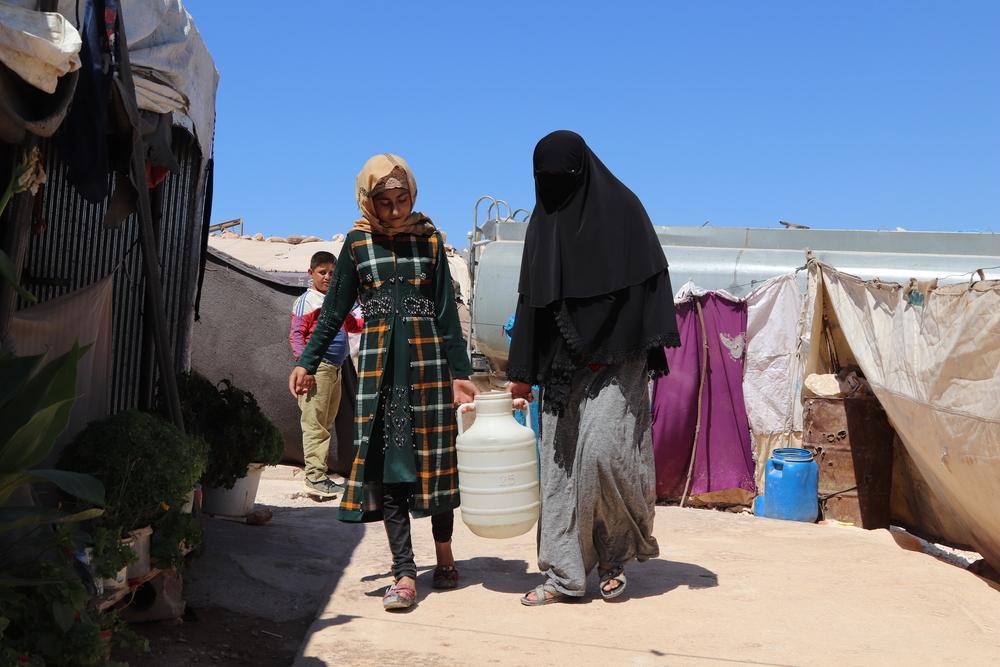 isplaced women carrying a pail of clean water provided by MSF in a camp in northwest Syria. 