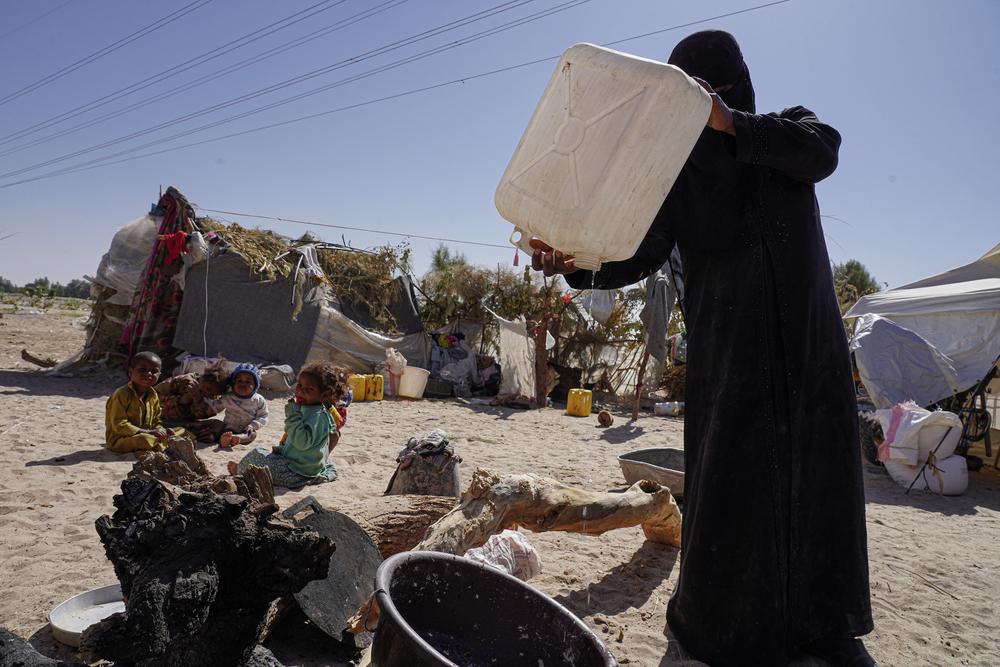 A woman pours the last drops of water from a bottle to prepare food next to her tent in the Al-Khuseif camp for internally displaced people in Marib, Yemen. 