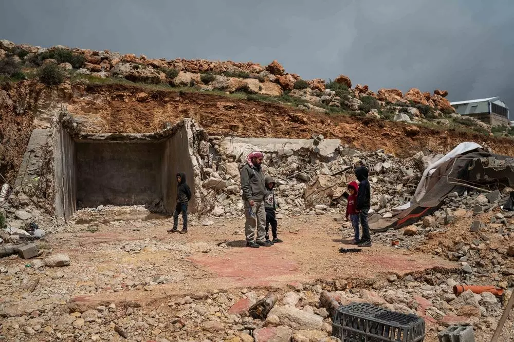 Mustafa Mlikat stands with his children next to the rubble of his house demolished by Israeli forces, in Douma. Palestine, April 2023. © Samar Hazboun