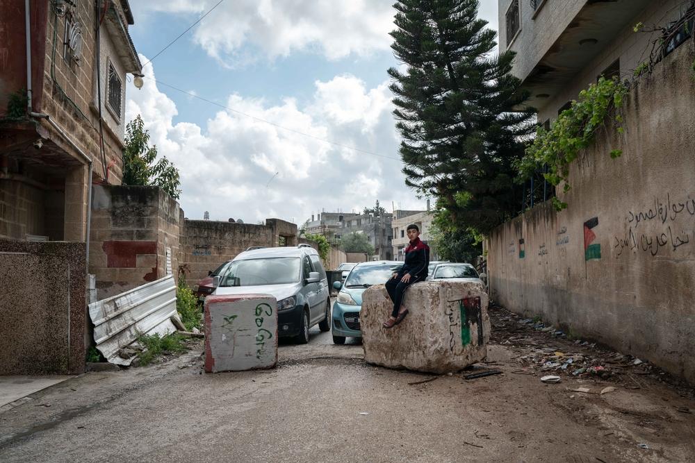 Hussam Odeh sits on a road block placed by Israeli soldiers in his neighborhood outside his home in Huwara. Palestine, April 2023. © Samar Hazboun