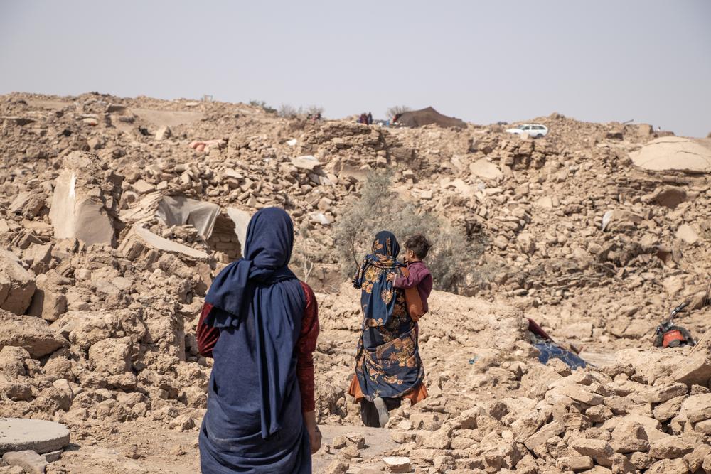 Two women and a child walk past destroyed houses in Cha Hak Village, Injil District, Herat Province. All houses in the village were destroyed. Afghanistan, 2023. © Paul Odongo/MSF