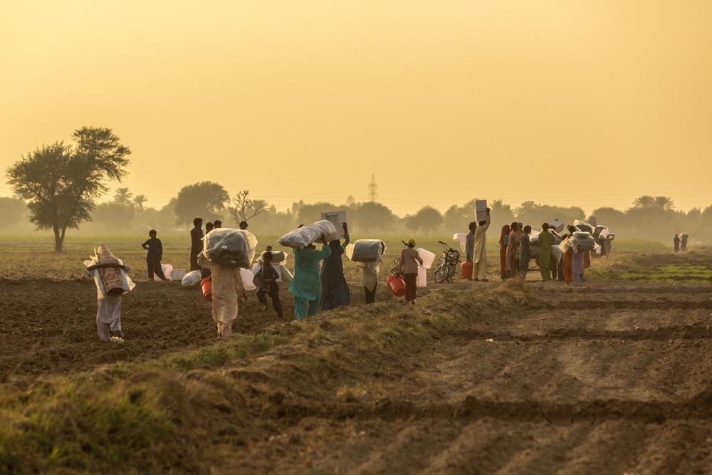 Villagers carry items, including blankets and cooking items, as they walk back to their homes at a village near Sanghar, following severe flooding in the country. Sindh province, Pakistan, November 2022. © Asim Hafeez for MSF