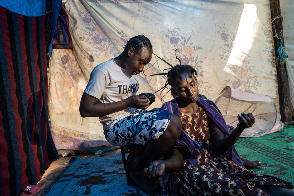 Kati Abati braids Fidtma’s hair. Both women have taken refuge in Mielizi displacement camp from floods, first in Cameroon, and now in the Chadian capital, N'Djamena. Chad, December 2022. © Fausto Podavini