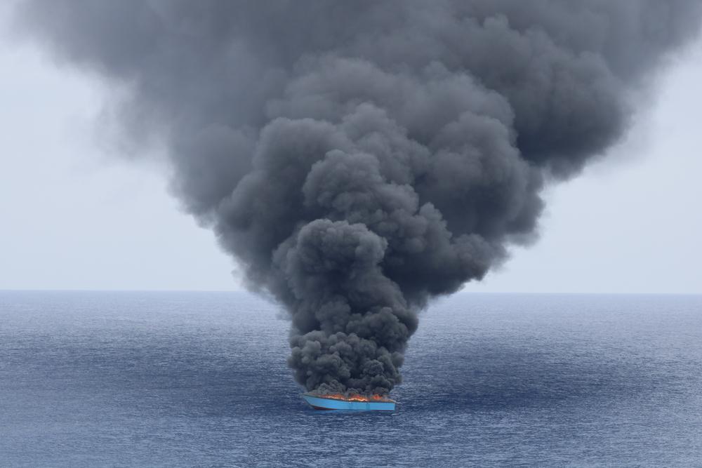Black smoke billows from a wooden boat after being intercepted by the Libyan Coast Guard. The boat had around 50 people onboard, who were transferred to the Coast Guard’s vessel before the wooden boat was set on fire. Central Mediterranean Sea, June 2023. © Skyi Mckee/MSF