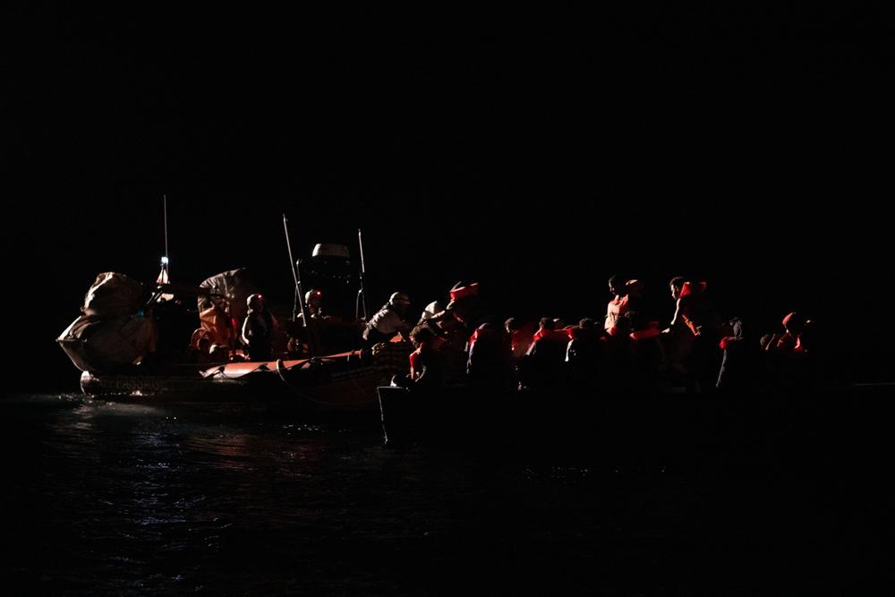 A team from the MSF search and rescue ship Geo Barents provides life vests to survivors on a wooden boat during a night-time rescue. Central Mediterranean Sea, July 2023. © Michael Rizzotti/MSF