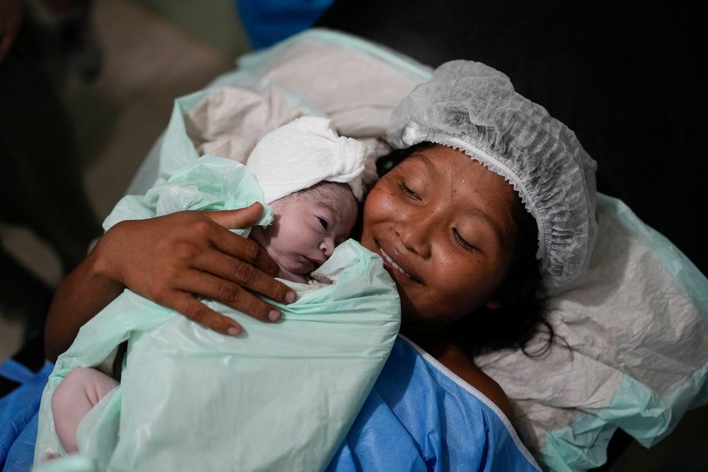 Adelia smiles as she holds her son José Antonio on her chest. After hours in labour, she feels exhausted, but is overjoyed at having her newborn baby in her arms. Delta Amacuro state, Venezuela, May 2023. © Matias Delacroix