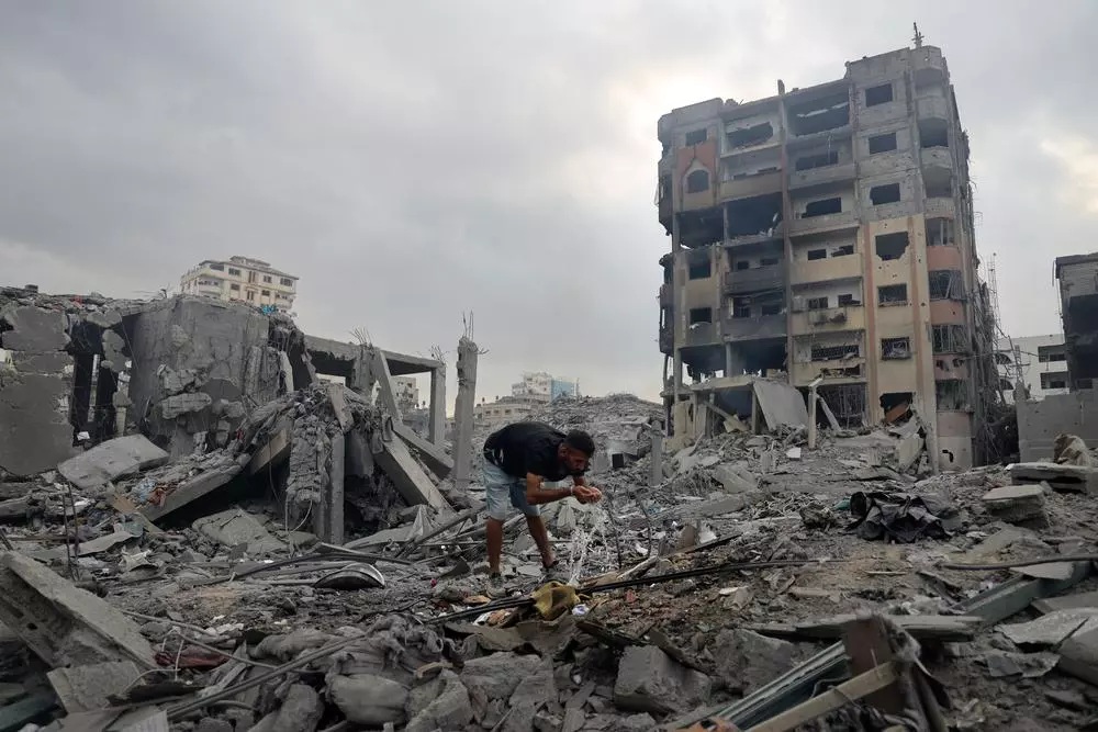 A man drinks water from a burst pipe amongst destroyed buildings in Gaza, following the outbreak of war between Israel and Hamas three days earlier. Gaza Strip, Palestine, 10 October 2023.  © Mohammed Baba
