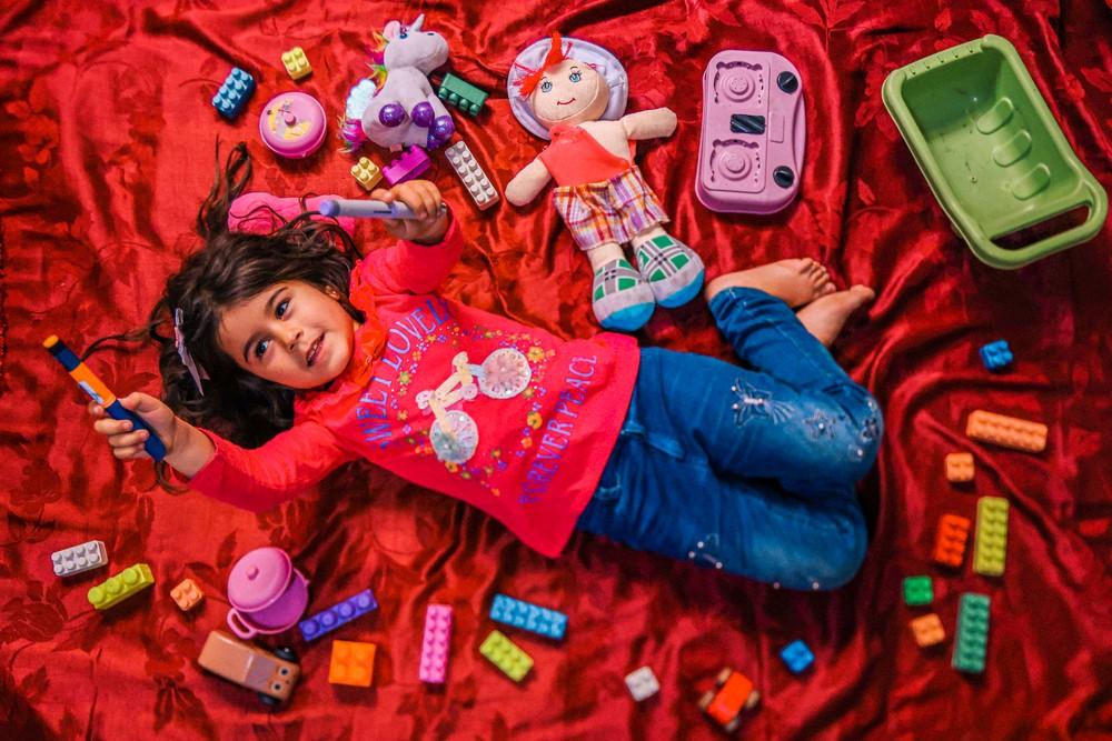Siwar holds up her insulin pen while lying down amongst her toys in her family’s makeshift home in Arsal. She was diagnosed with type 1 diabetes at a young age and frequents the MSF clinic in the town for treatment. Arsal, Lebanon, May 2023. © Carmen Yahchouchi/MSF