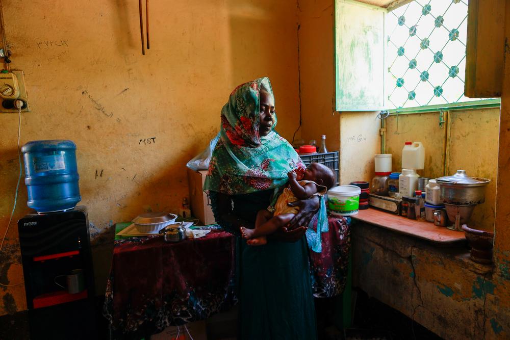 Souad Abdullah, a displaced woman from south Khartoum, holding her baby in Al Zahra Camp, Al Jazirah State where she takes refuge. Sudan, December 2023. © Fais Abubakr