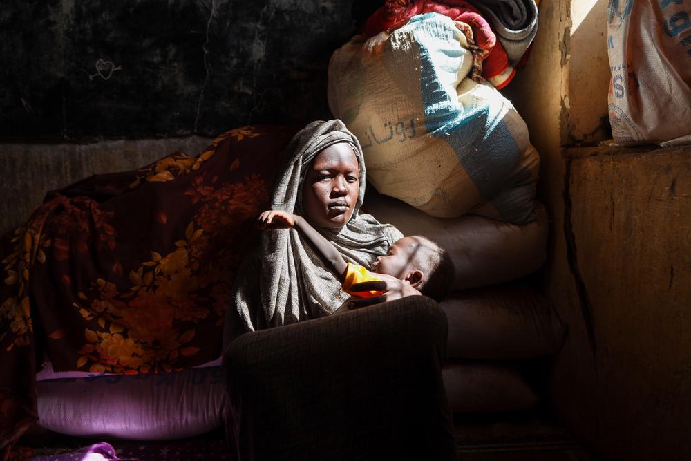 A displaced woman holds her child as she takes refuge in Alsafat Camp in Al Jazirah state. Sudan, December 2023. © Fais Abubakr