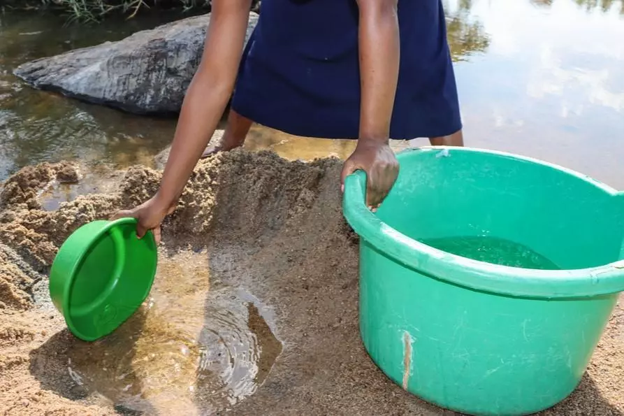 A woman is digging small holes to fetch water at rio Meluli, Mozambique