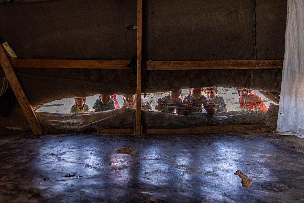 Syrian refugee children peak through the ventilation opening of a tent.
