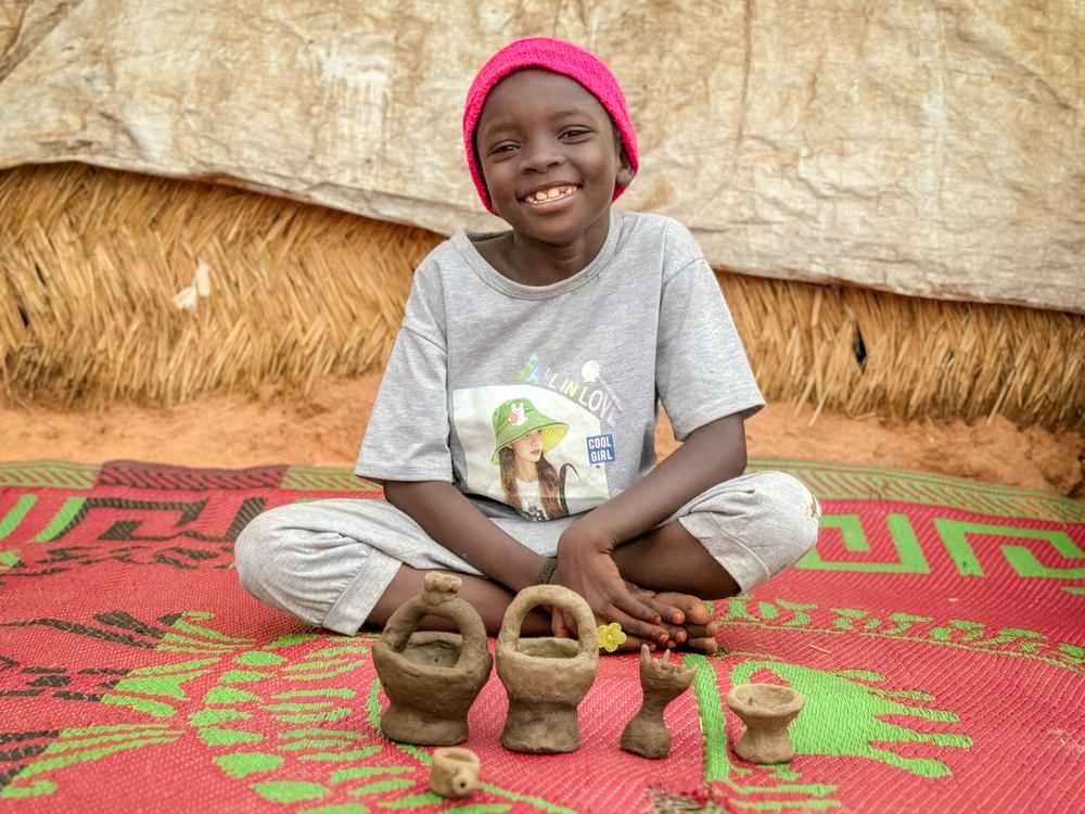 A Sudanese child poses in front of little cups and tea pots she makes from mud she picks up after the rain in Adre refugee camp. Chad, July 2024. © Thibault Fendler/MSF