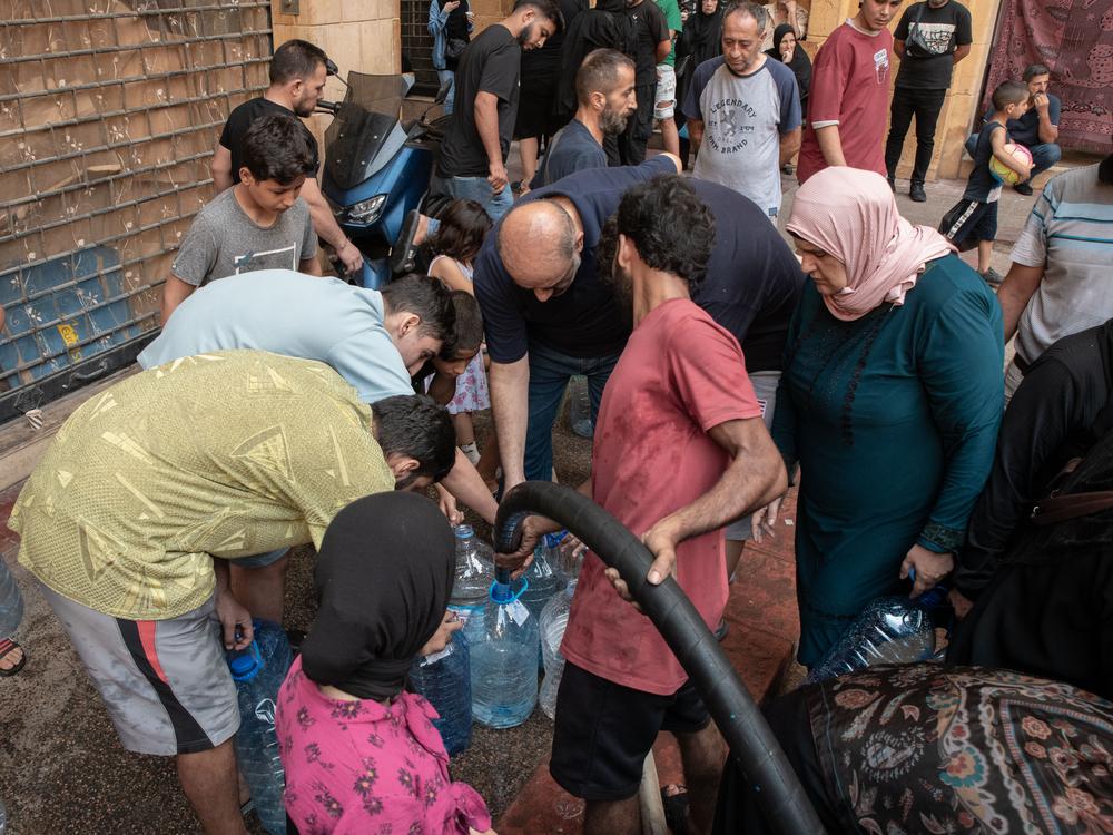 Displaced families from the Azarieh shelter crowd around a water tank during a water distribution. Lebanon, October 2024. © Antoni Lallican/Hans Lucas