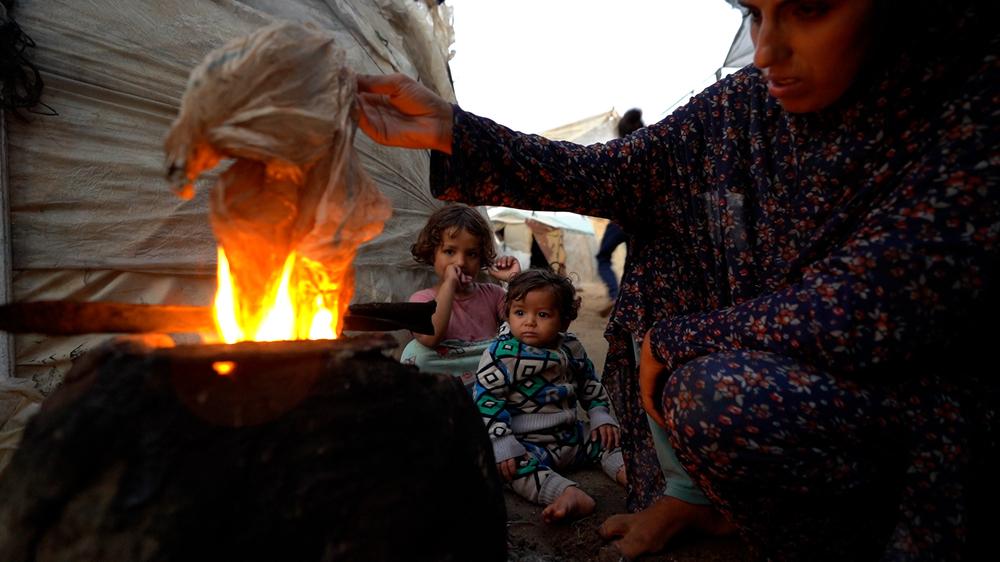 With no access to cooking gas, a mother is forced to light a fire using plastic to prepare a meal for her children, finding alternative ways to feed her family in dire conditions.