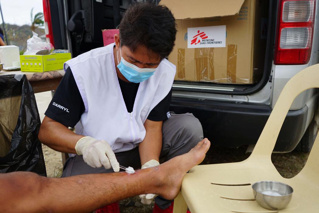 Nurse Daryll Von Abellon cleans a leg wound on a teenaged boy. Philippines, November 2024. 