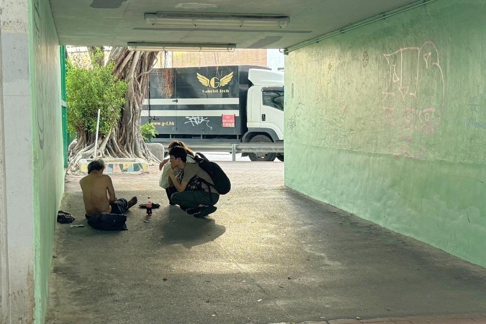 An MSF staff engages with a person experiencing homelessness in a shaded underpass in Hong Kong.