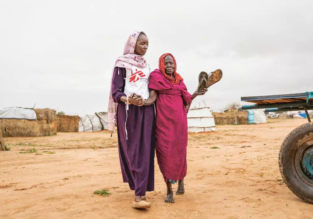Health promoter accompanies an 80 year old patient to the MSF clinic in Adré transit camp, eastern Chad. 