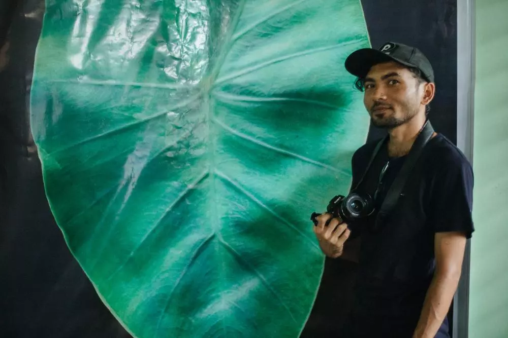A Rohingya man standing in front of taro leaf artwork symbolising Rohingya refugee experience