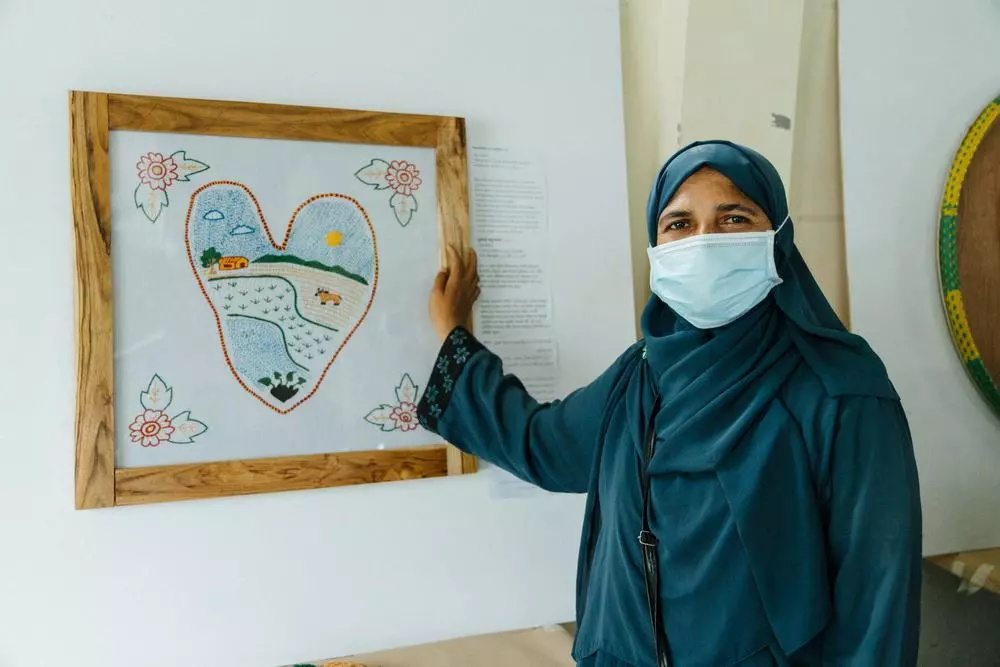 A Rohingya woman standing in front of taro leaf artwork symbolising Rohingya refugee experience