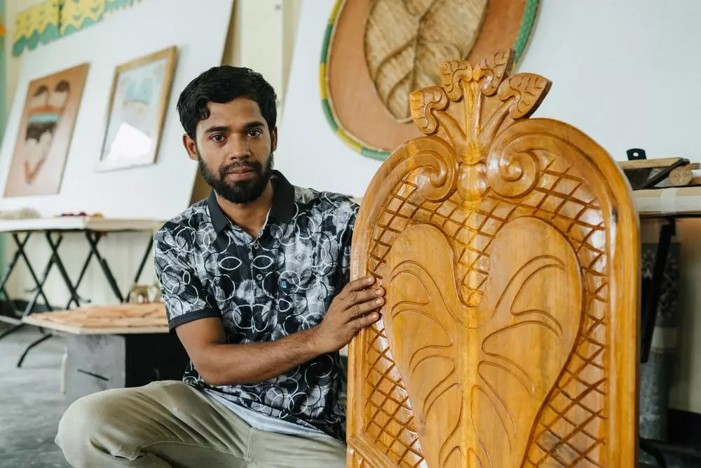 A Rohingya man standing in front of taro leaf artwork symbolising Rohingya refugee experience