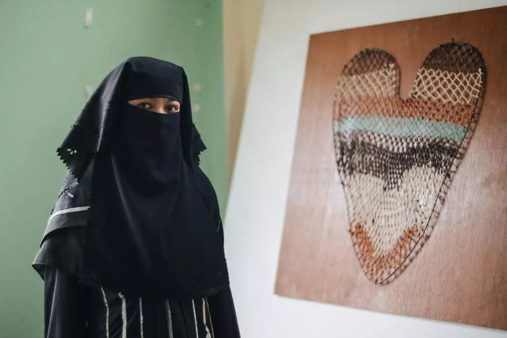 A Rohingya woman standing in front of taro leaf artwork symbolising Rohingya refugee experience