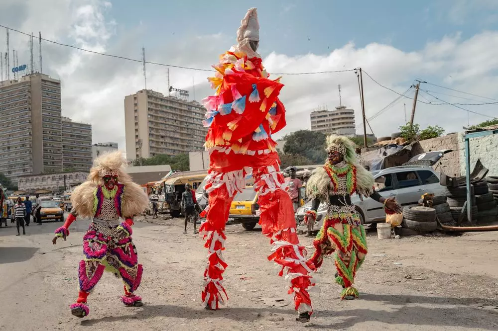 Artists in traditional false lions costumes and stilt walkers interact during the "Clima Yaakaar" music video shoot in Reubeuss