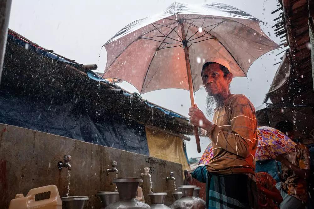 A Rohingya refugee shelters under an umbrella during heavy rain