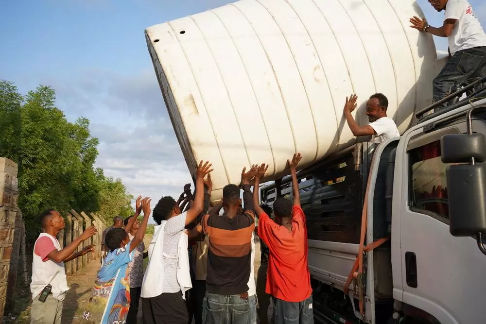 MSF staff and community members install a water tank at a displaced people’s camp