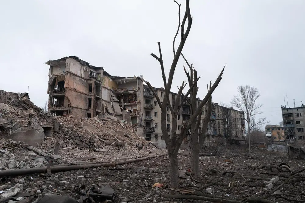 roken trees stand amid rubble near a destroyed residential building